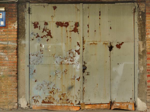 Large aged beige doors with crumbling paint and rusting surface.